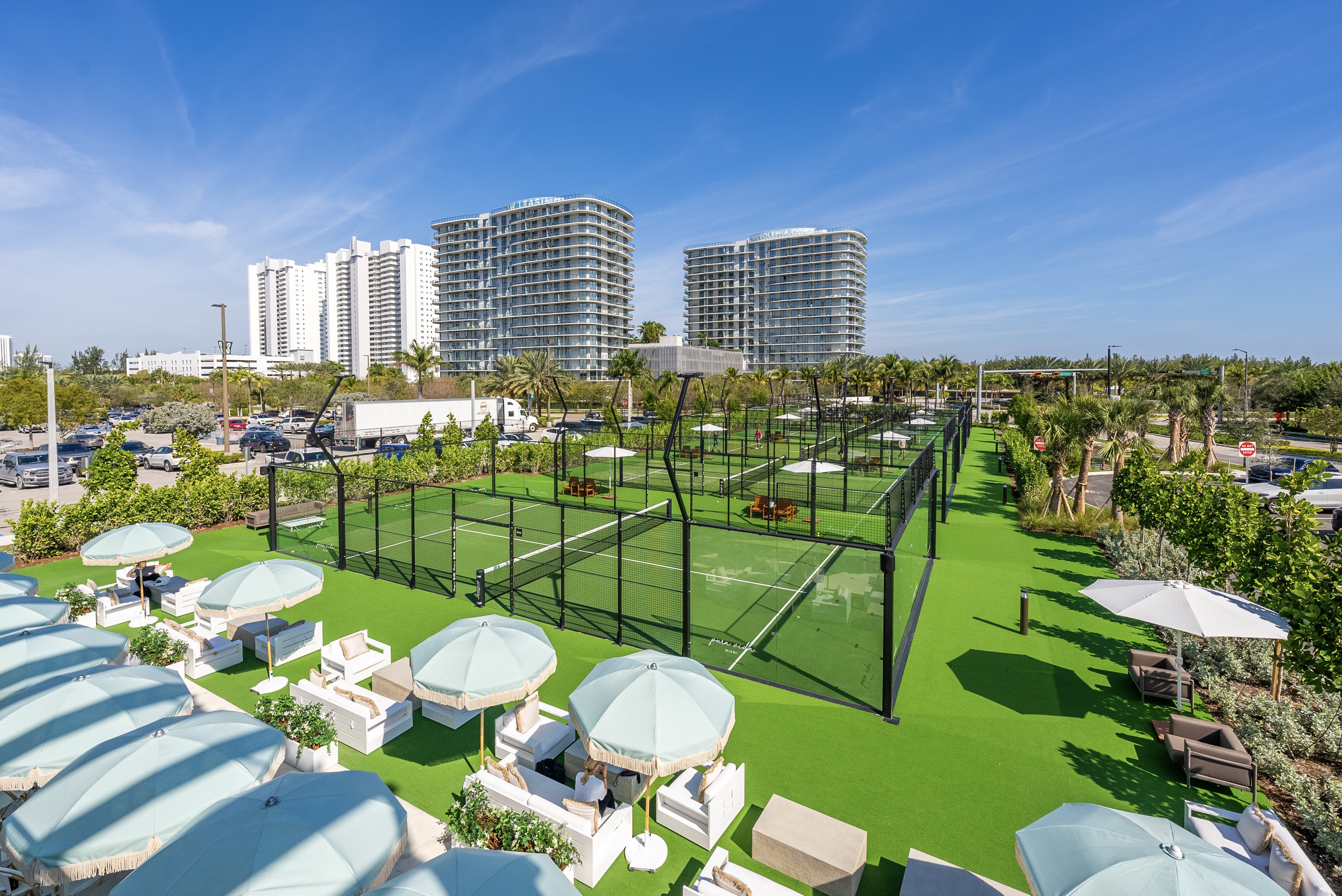 A tennis court surrounded by green grass and white umbrellas.